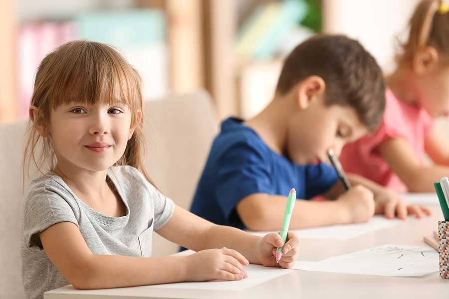children sitting at a table and writing or drawing