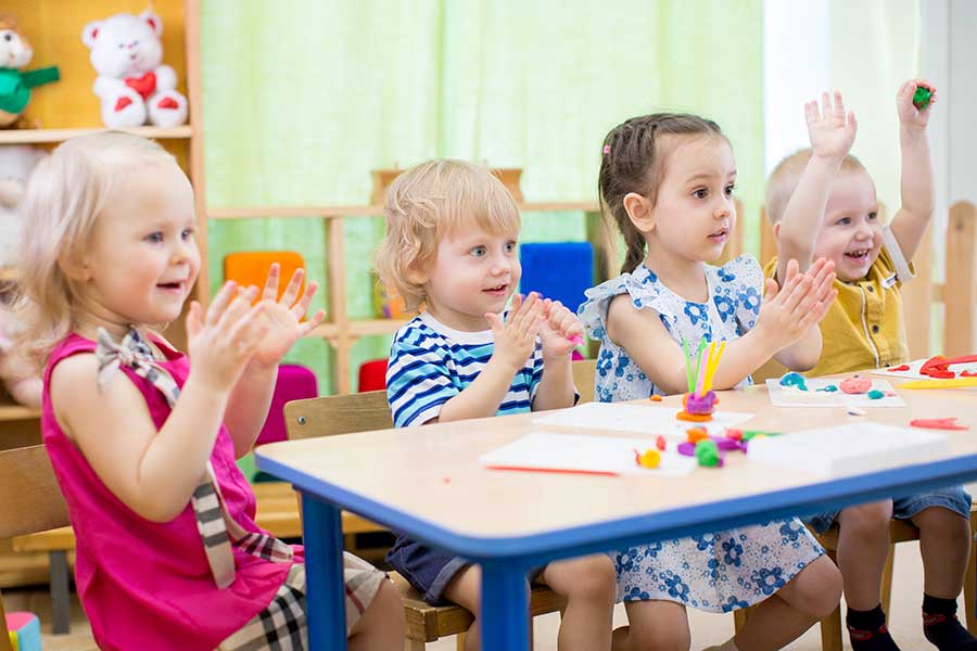 group of preschoolers clapping and sitting at a table